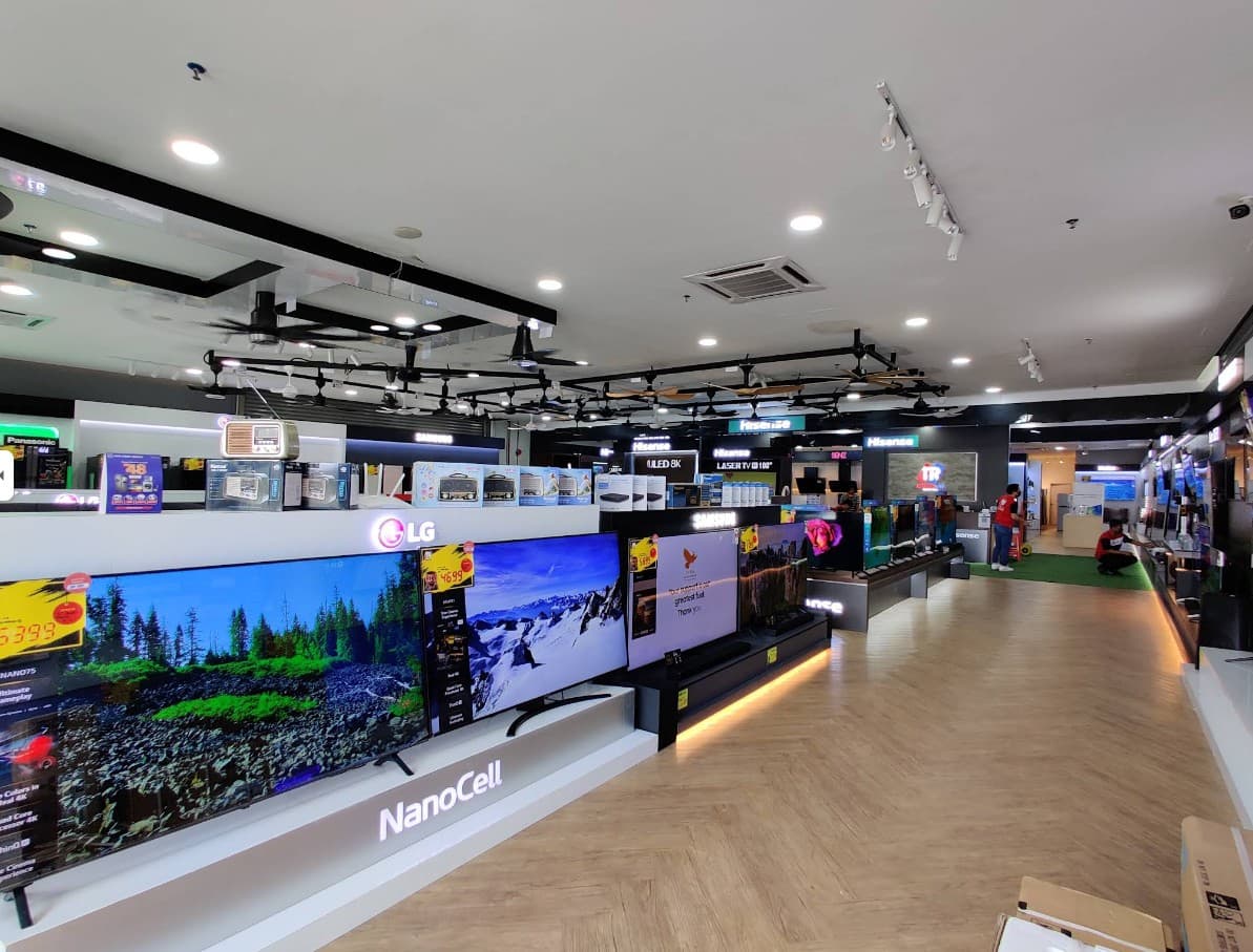 Tanradio 分行内部 — 排列整齐的 LG、Samsung、Hisense 与 Panasonic 电视，前景是洗衣机，天花板上展示着风扇。